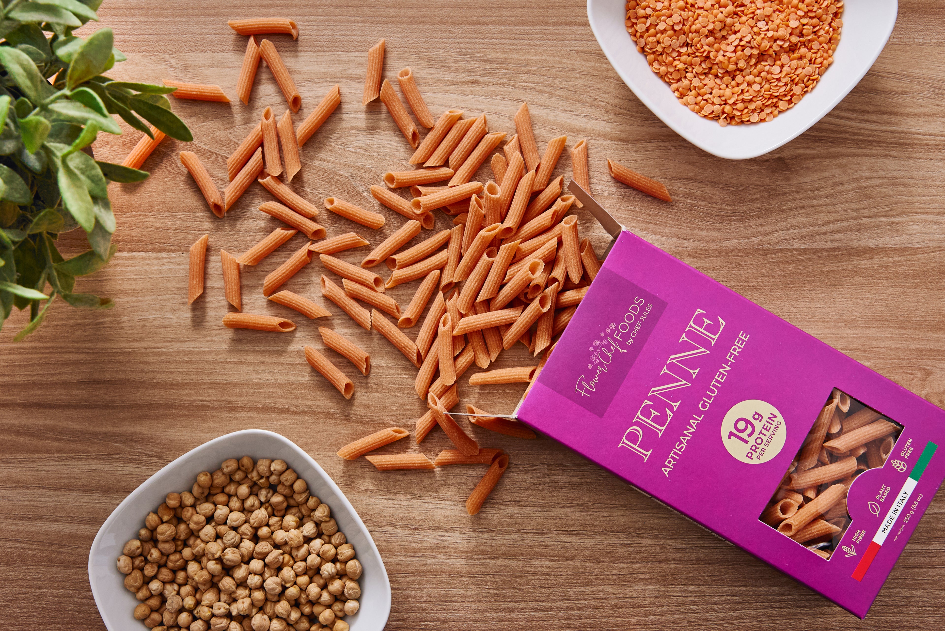 Our Story | Flower Chef Foods Gluten-Free Pasta_ Penne pasta on a wooden surface with a box of Penne pasta and bowls of lentils.
